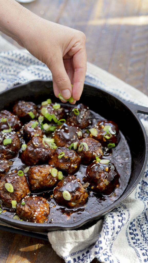 Sprinkling scallions on a pan of meatballs