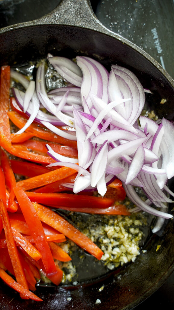 Peppers and onions in a skillet with garlic and greek chicken marinade.