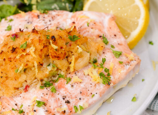 Crab stuffed salmon recipe on a plate with lemon and a spinach salad.