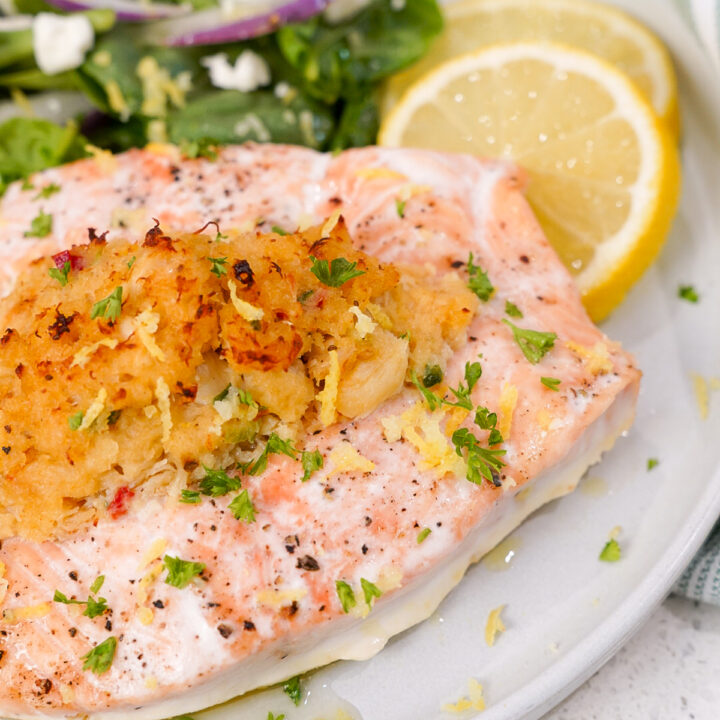 Crab stuffed salmon recipe on a plate with lemon and a spinach salad.