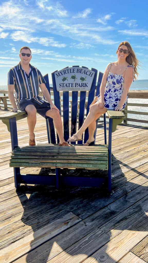 Both Karen and Gavin sitting on a big chair on the boardwalk in Myrtle Beach in the fall.