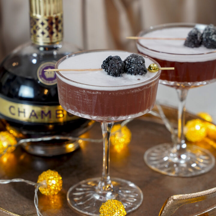French martini cocktail with a bottle of chambord on a tray with berries as a garnish.