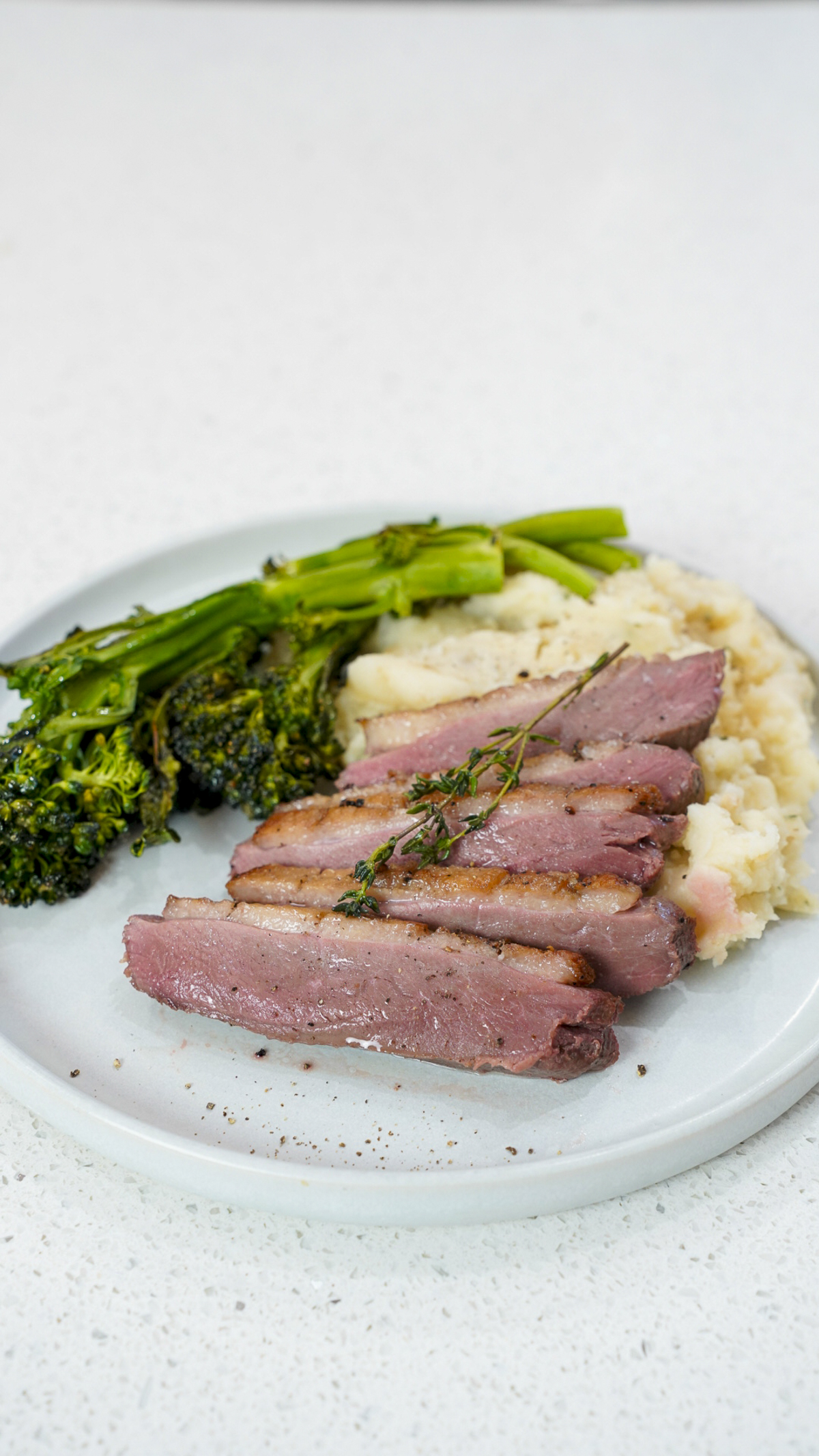 Juicy sous vide duck breast with crispy skin on a plate with mashed potatoes and broccolini.
