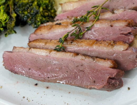 Juicy sous vide duck breast with crispy skin on a plate with mashed potatoes and broccolini.