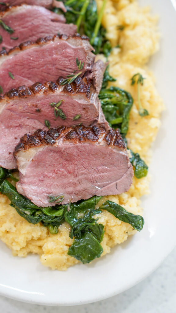 Duck breast served on a platter on top of a parmesan polenta recipe.