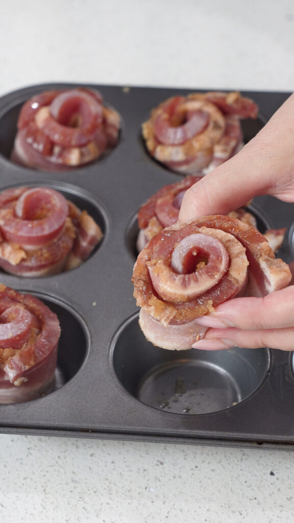 Candied bacon roses being placed in a muffin tin.