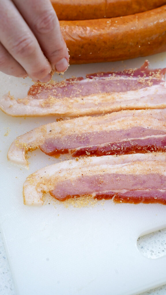 Speading brown sugar on a bacon slice for a pig shots recipe.