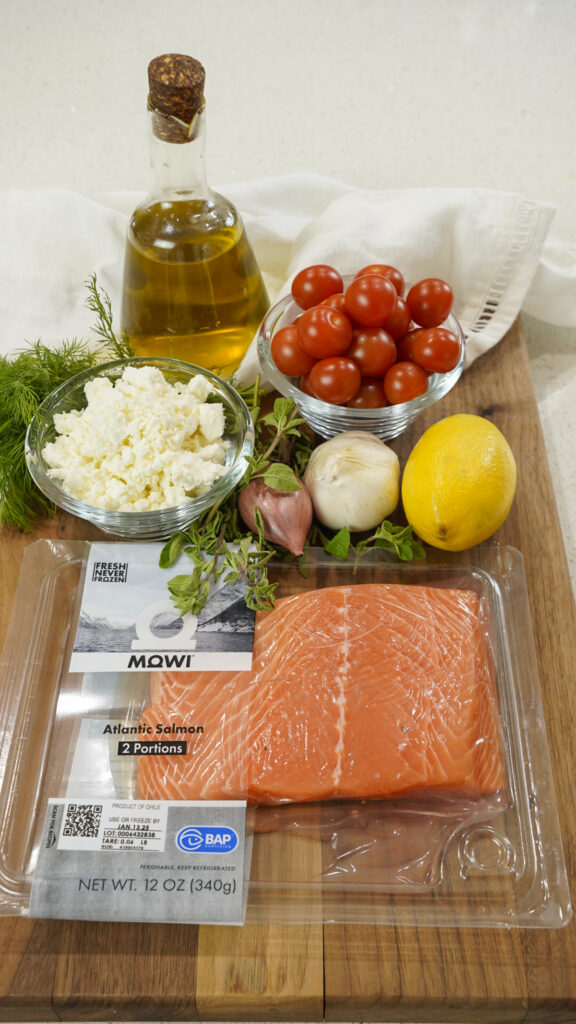 Cutting board with the ingredients for a baked Mediterranean salmon recipe.