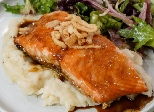 Finished Guiness glazed salmon recipe on a plate with mashed potatoes and salad.