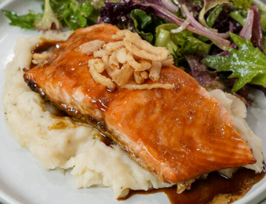 Finished Guiness glazed salmon recipe on a plate with mashed potatoes and salad.