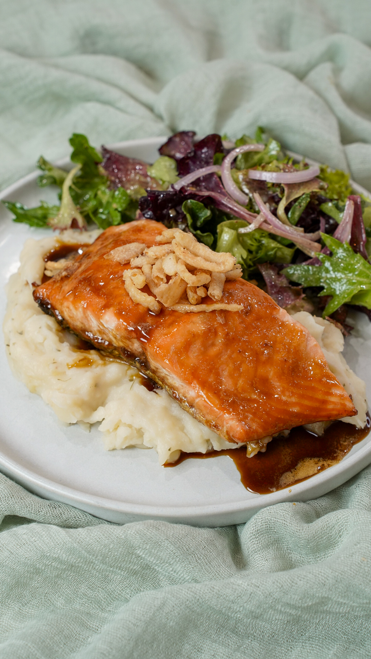 Finished Guiness glazed salmon recipe on a plate with mashed potatoes and salad.