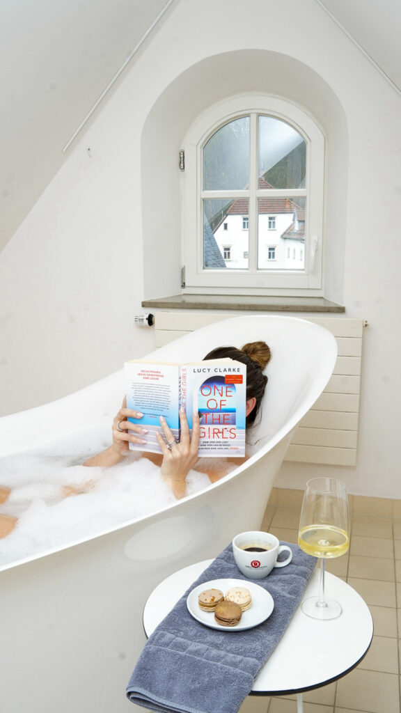 Woman reading a book in a bathtub at PostHotel in Germany.