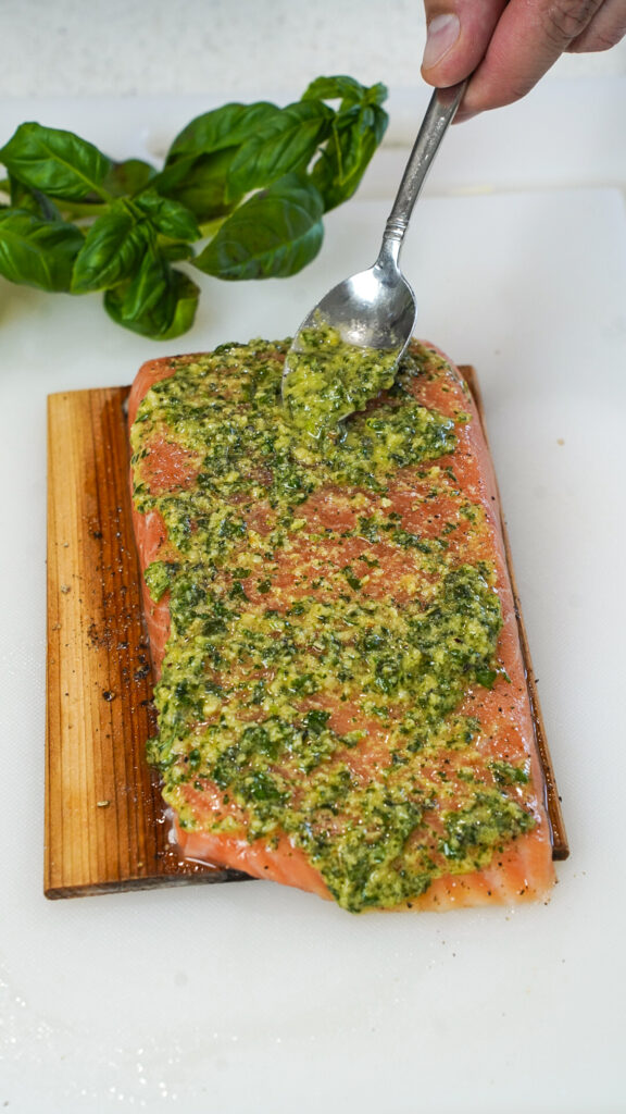 Spooning homemade pesto on salmon for a grilled pesto salmon recipe.