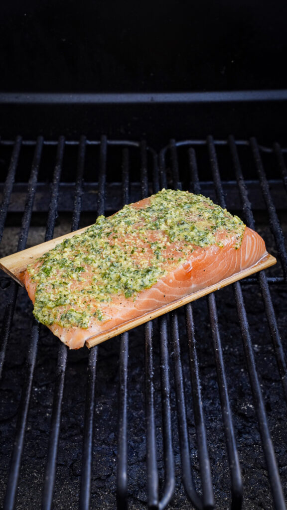 Salmon topped with homemade pesto for a grilled pesto salmon on a cedar plank on a grill.