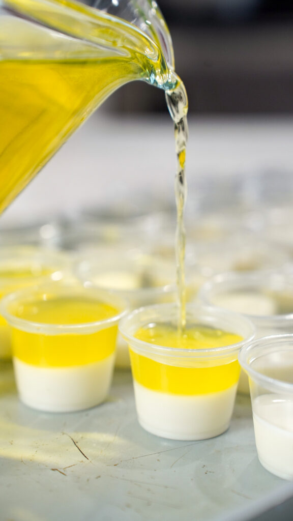 A yellow layer being poured into shot glasses for a Pina Colada Jello Shots Recipe.