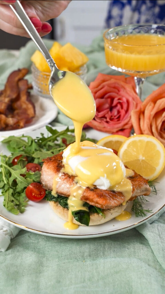 Homemade hollandaise sauce being spooned over a seared salmon eggs benedict recipe.