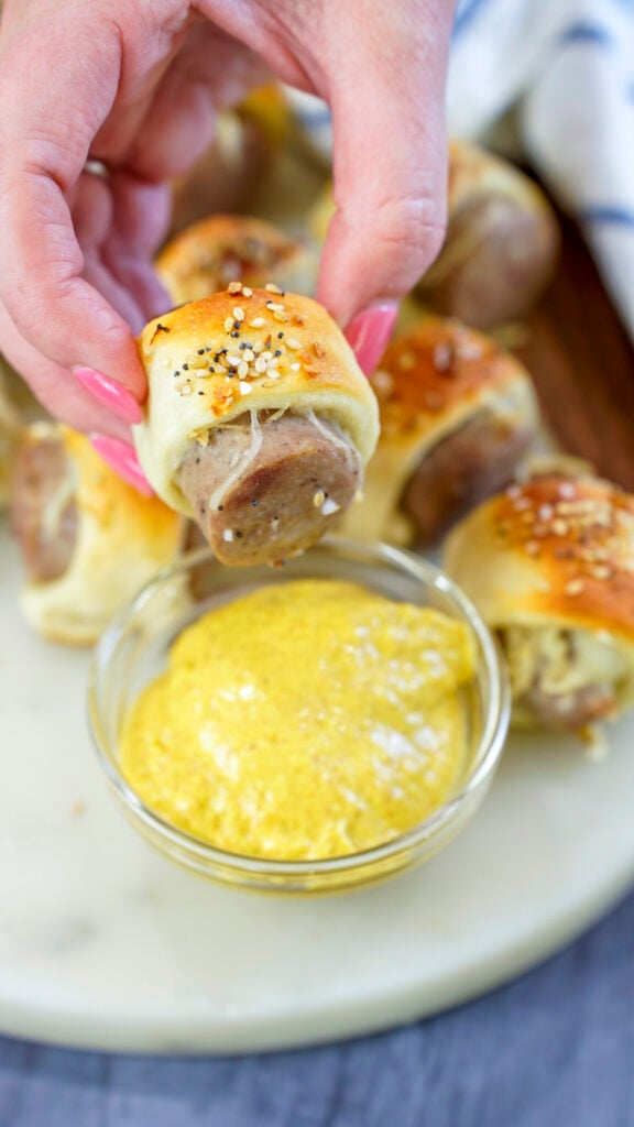Brats in a blanket recipe for an oktoberfest party being dipped into mustard.