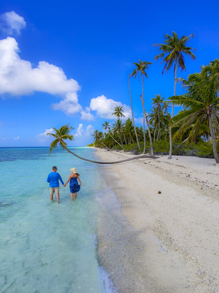 A couple walking by a palm tree in Fakarava, a stop on the Windstar Tahiti French Polynesia cruise.